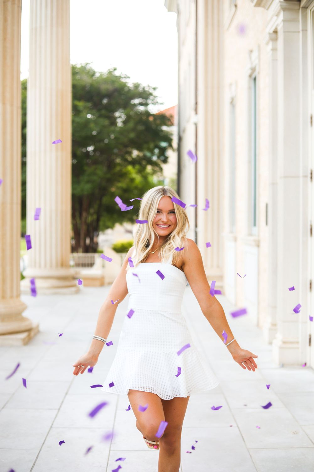 Purple confetti falling around person in white dress on collegiate steps.