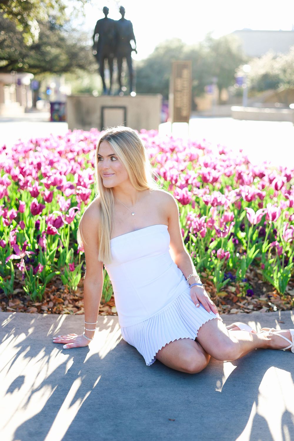 White dress photoshoot in garden with vibrant pink tulips and natural sunlight.