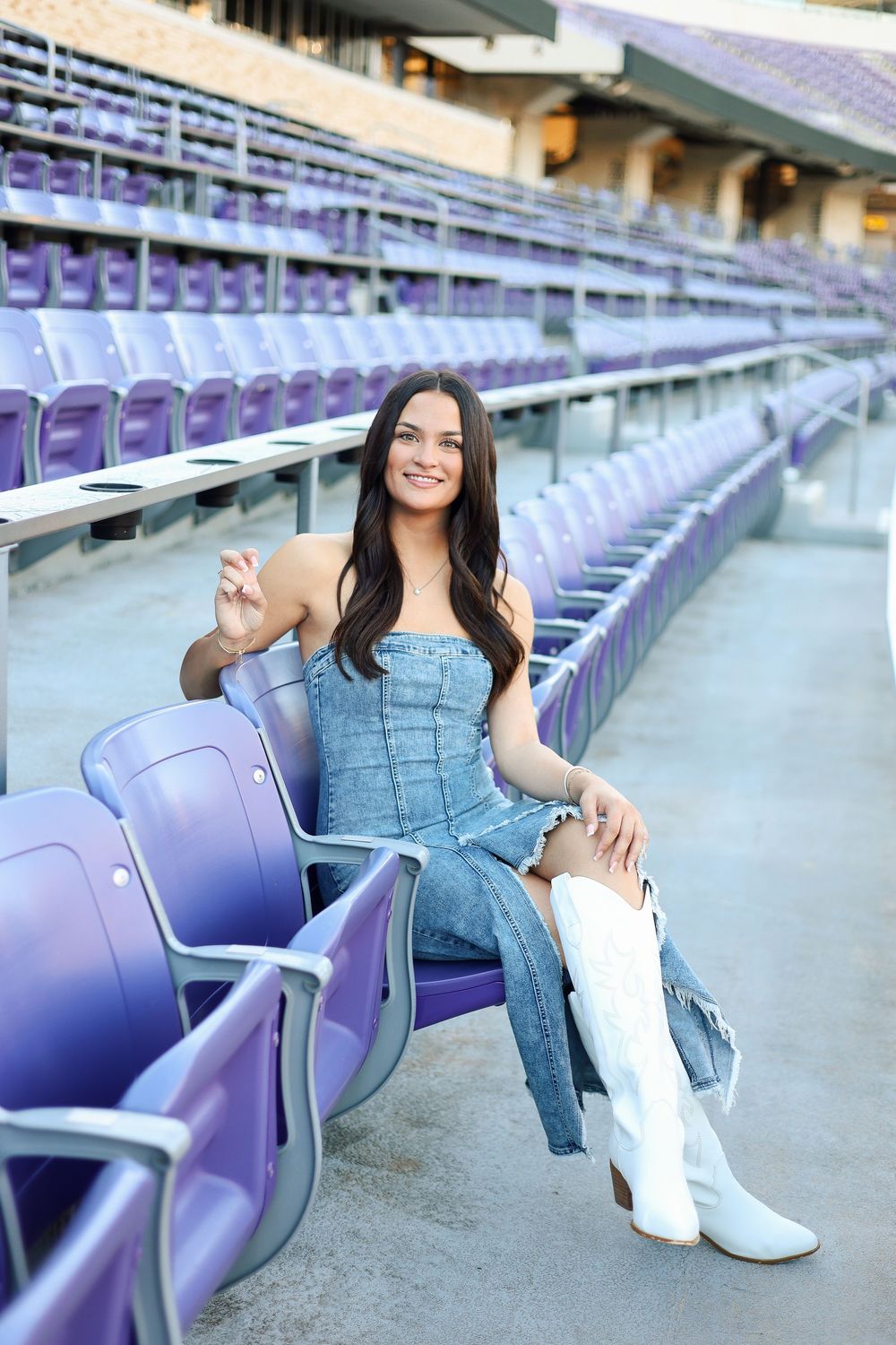 Stadium photoshoot featuring graduate in denim outfit and white boots among purple seats.
