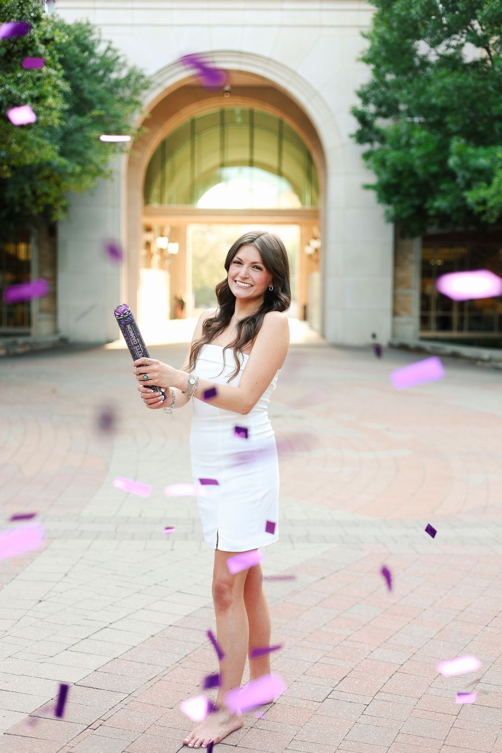 Graduate takes celebratory photos with purple confetti flying through the air.