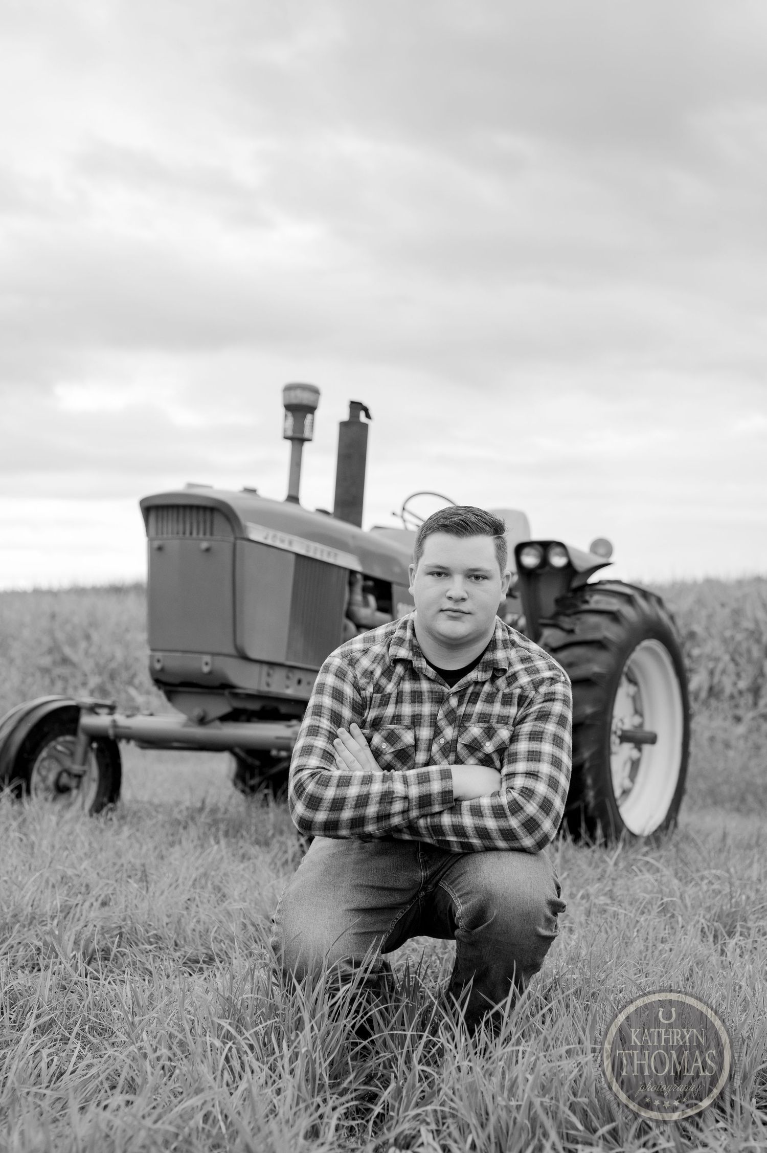 A person kneels beside a vintage farm tractor in black and white photography.