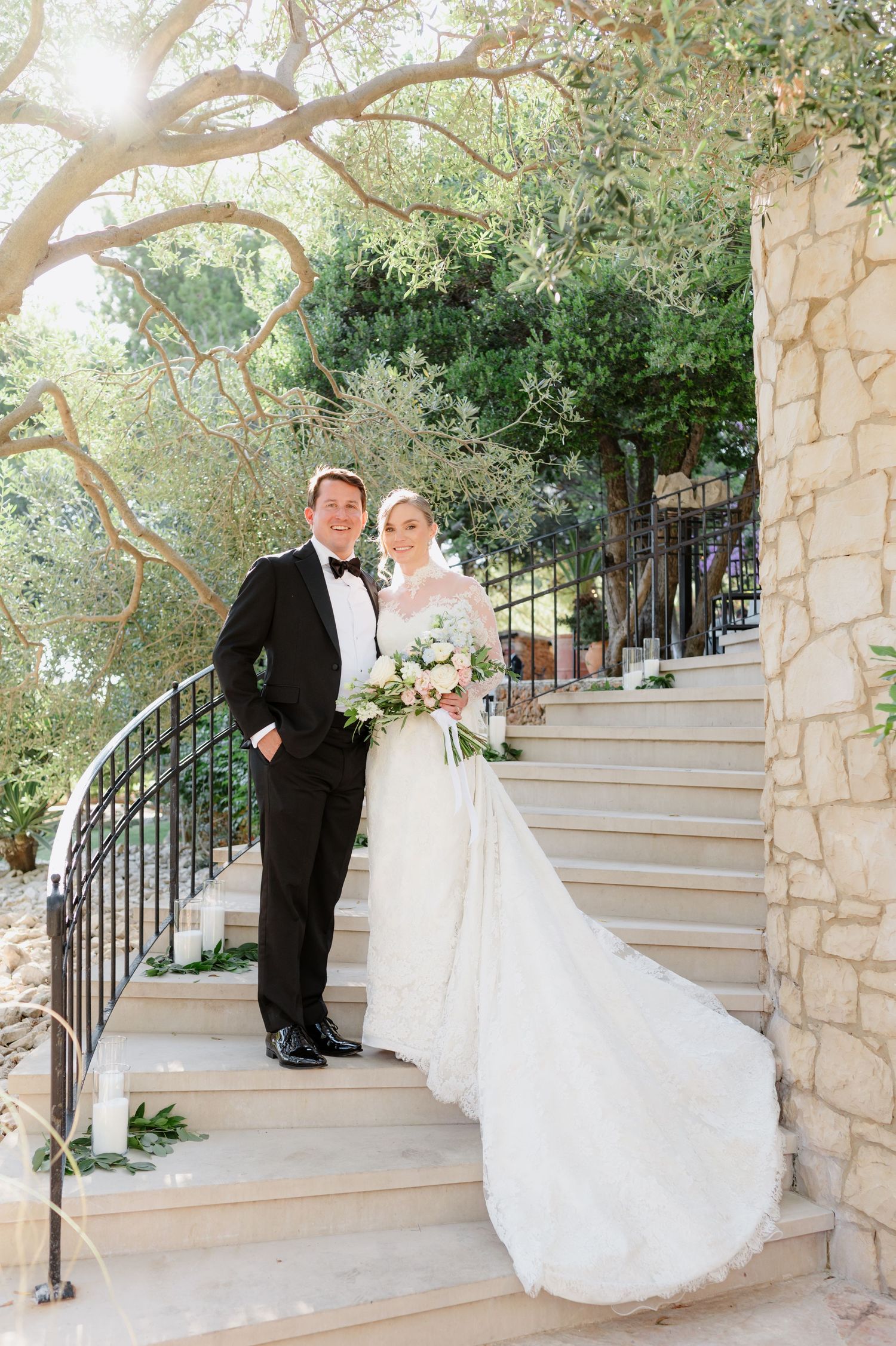 Elegant wedding portrait on stone steps with dramatic train and natural garden backdrop.