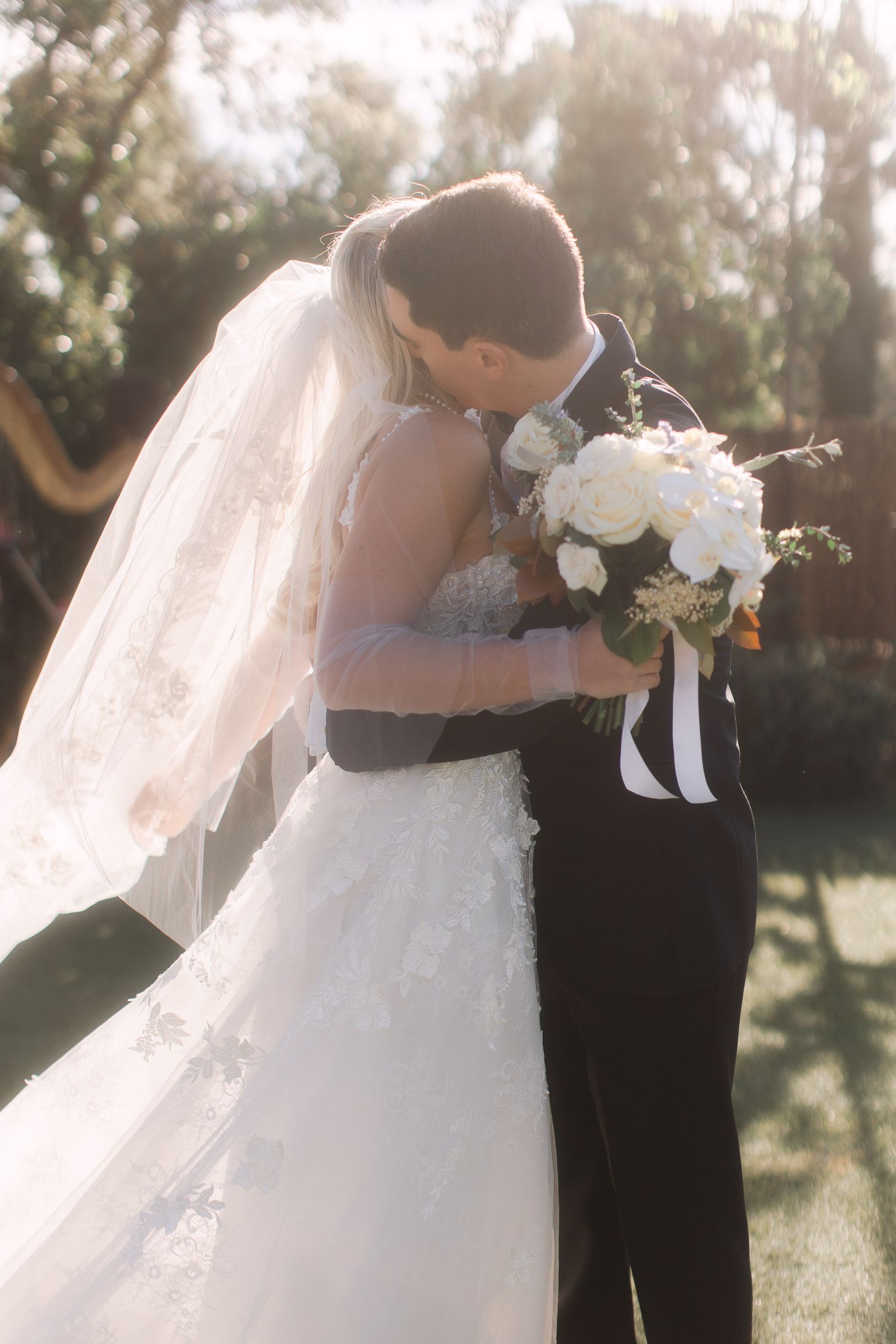 Sunlit wedding moment with bride holding white bouquet during outdoor ceremony.
