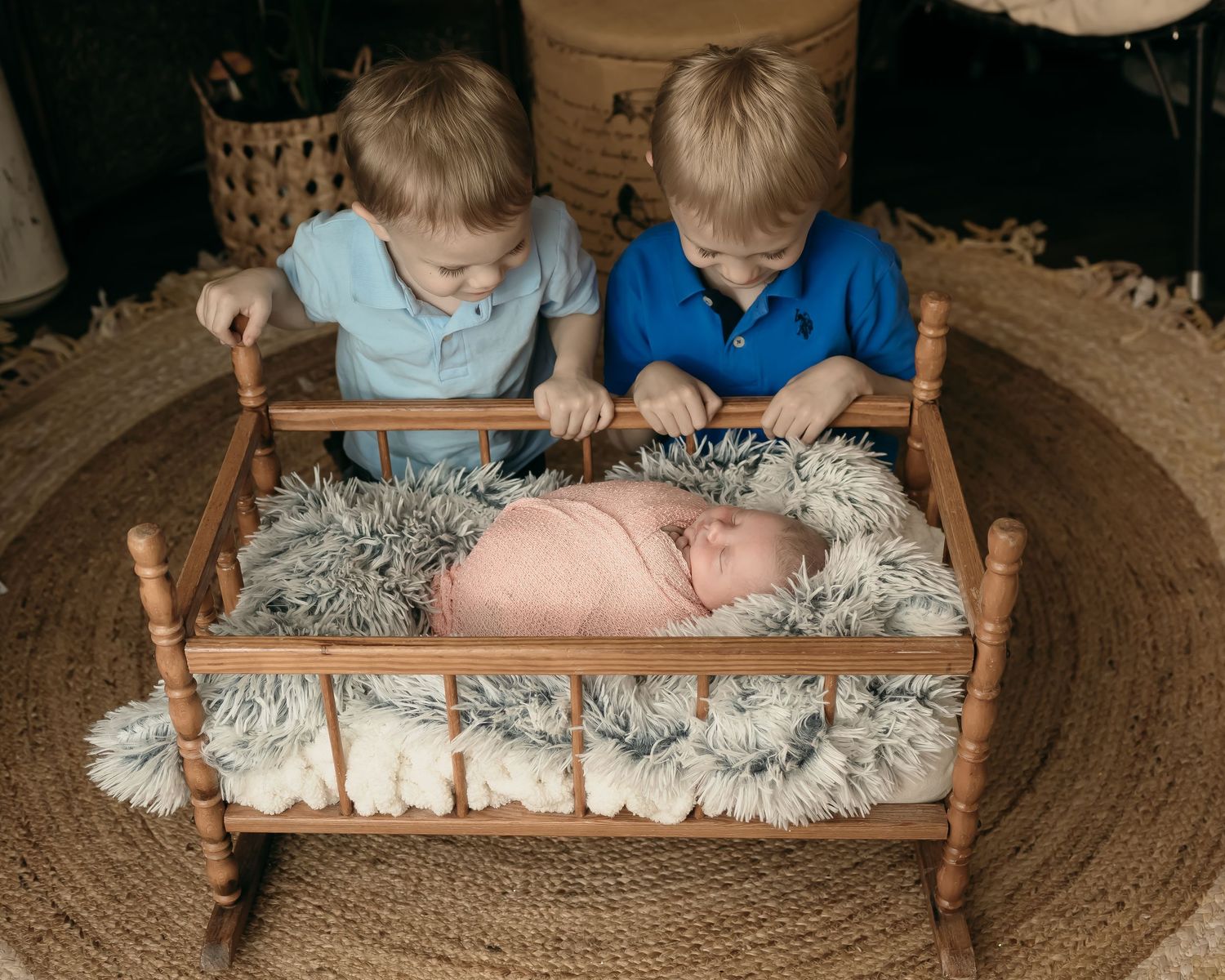 Two young children peer into a wooden crib containing a sleeping baby.