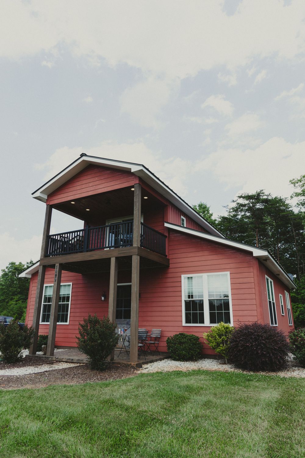 Modern coral-colored house with second floor balcony and landscaped front yard.