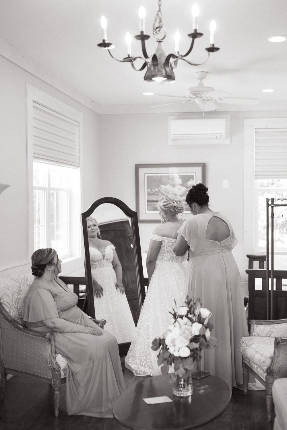 Elegant bridal preparation room with chandelier and wedding dress being fitted.