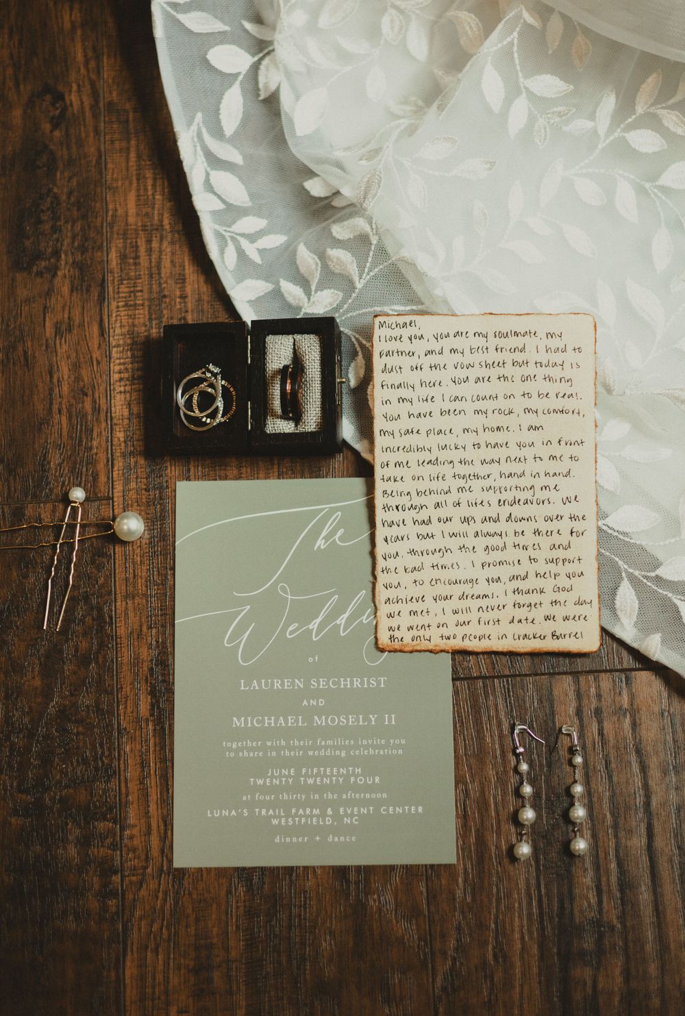 Wedding invitation and wedding details flatlay with lace and jewelry on dark wooden background.