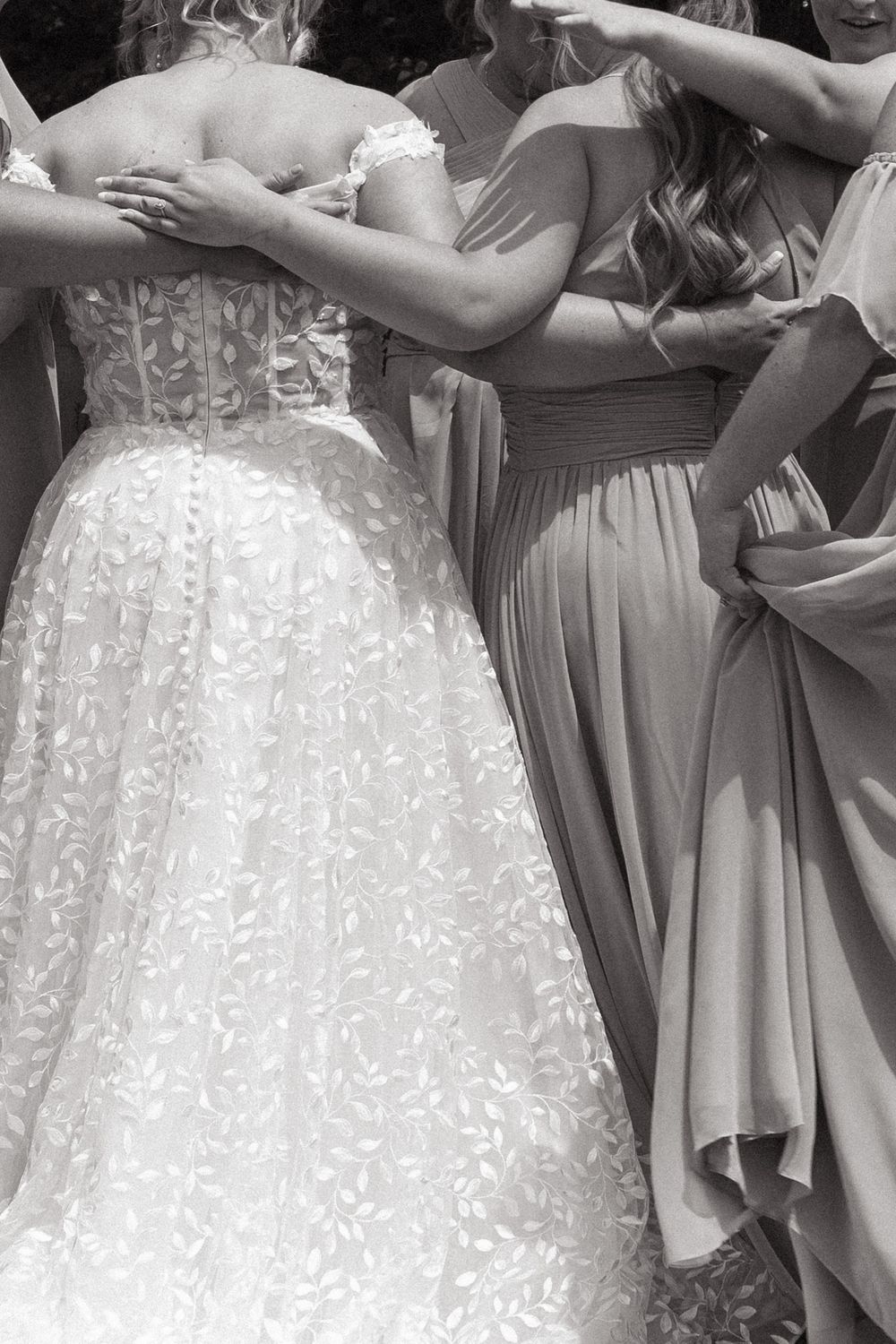 Close-up black and white photo showing the intricate lace details of a wedding dress and bridesmaid gown.