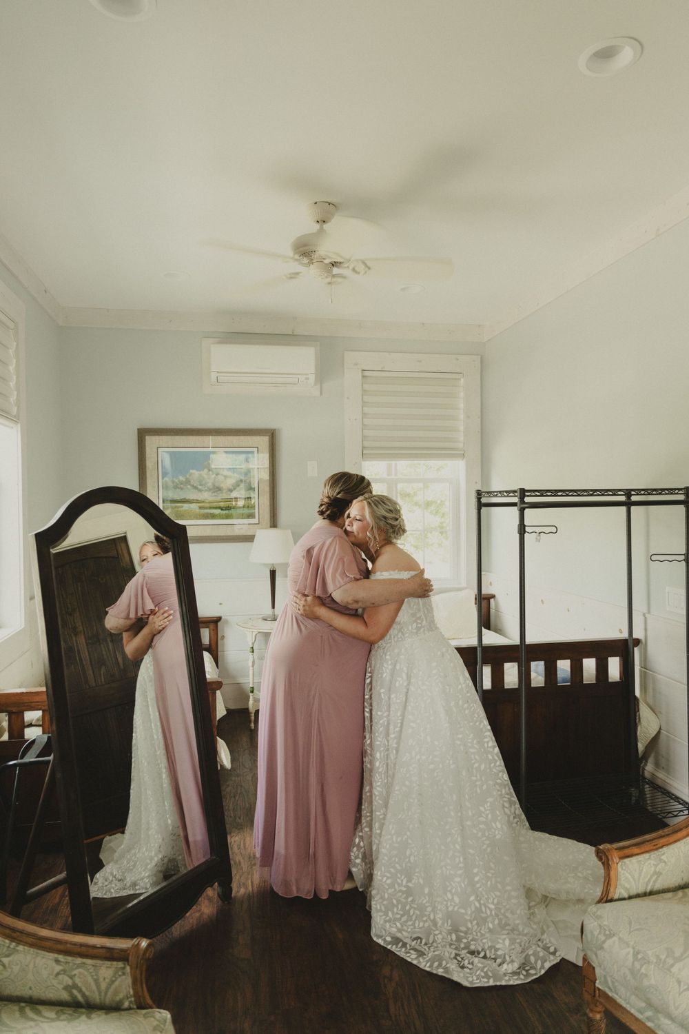 An emotional moment captured in a bridal suite with two people embracing in formal dresses.