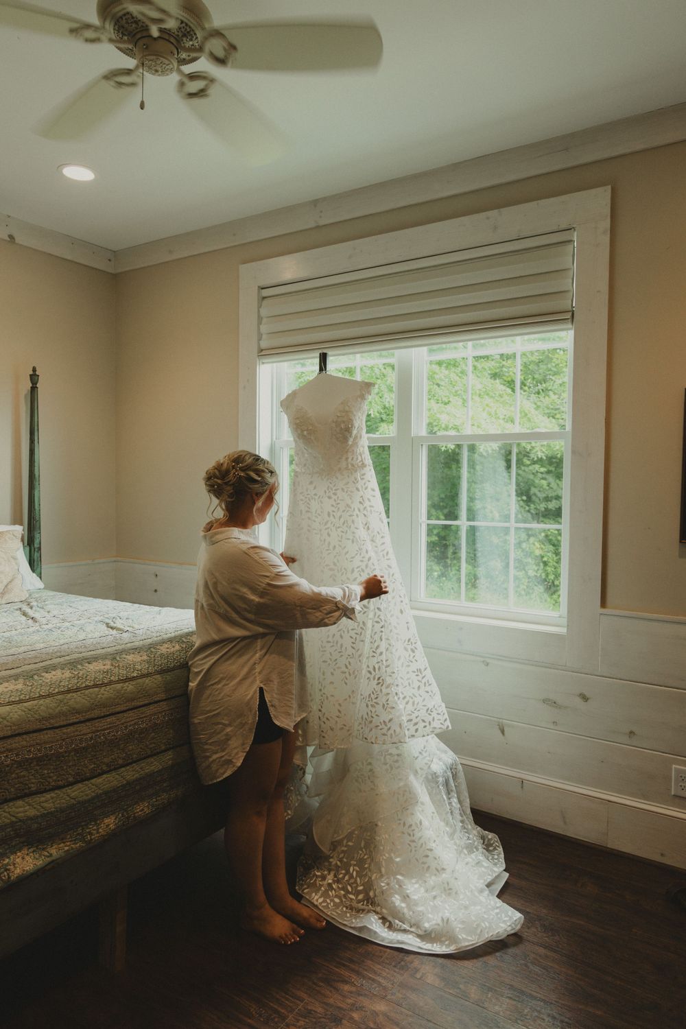 A beautiful lace wedding dress being steamed by window in a sunlit room.