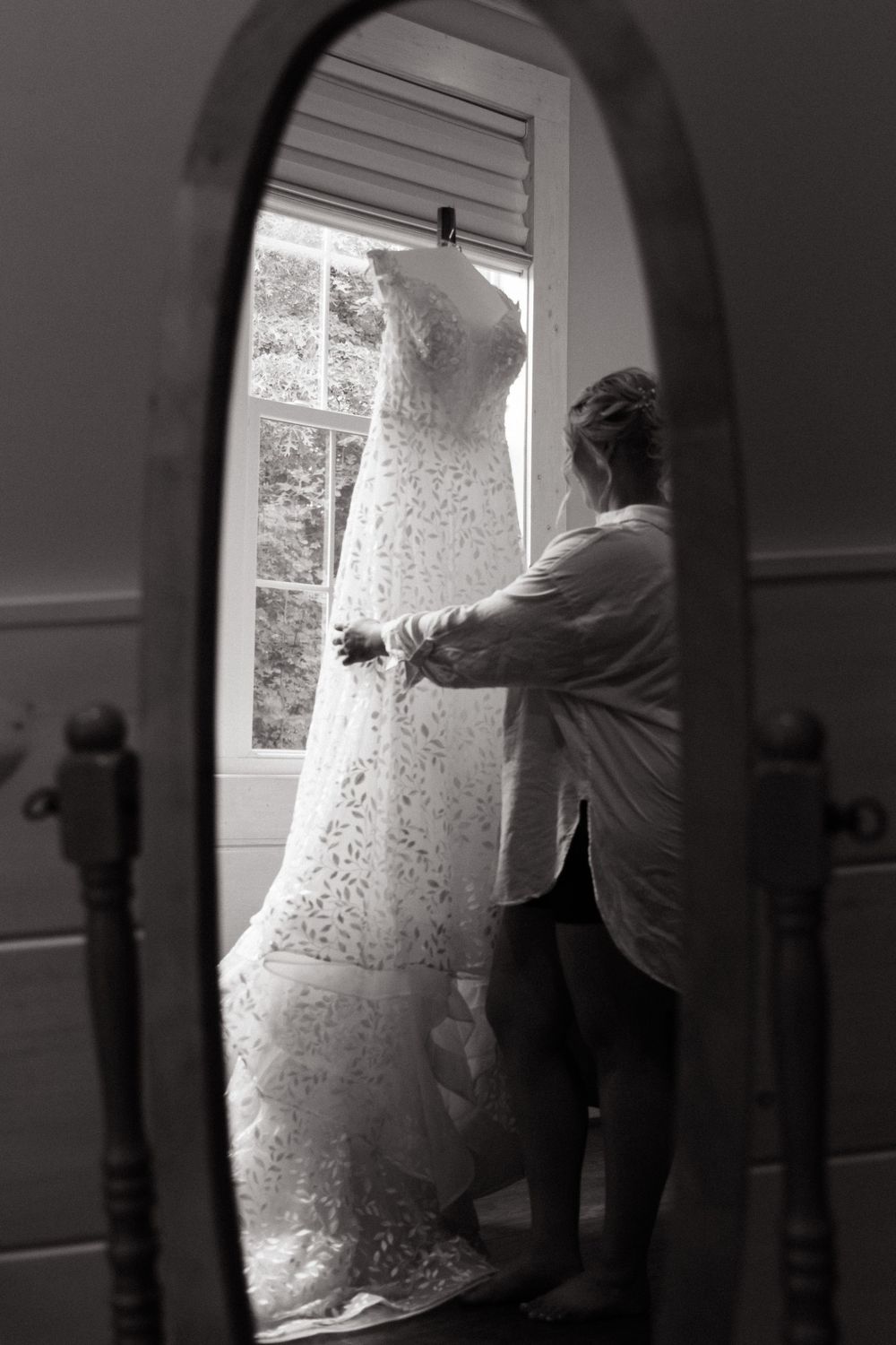 Mirror reflection of wedding dress preparation by a window in black and white.