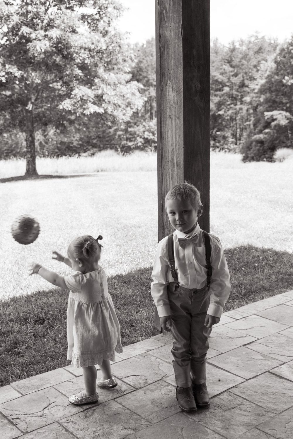 Vintage black and white photo of two children on a porch playing with a ball.