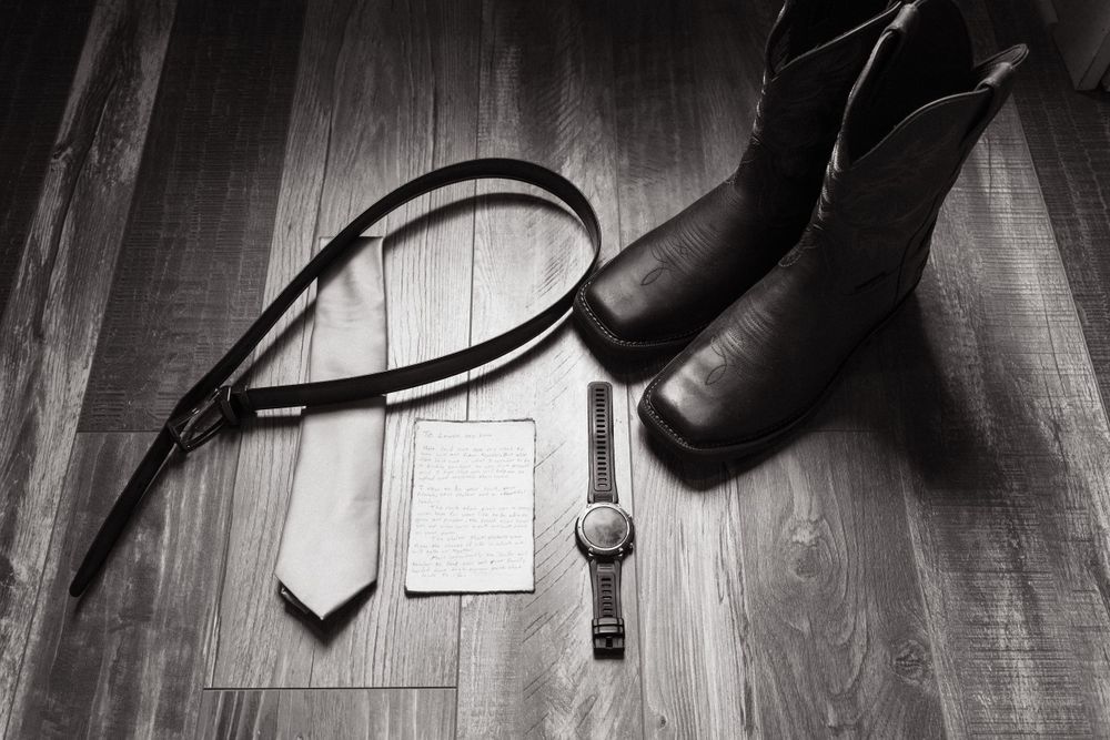 Flat lay of black boots, watch, and cell phone on wooden flooring.