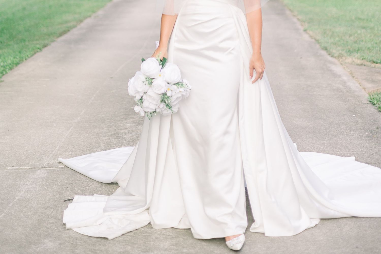 Bride in white dress poses gracefully on outdoor garden pathway.