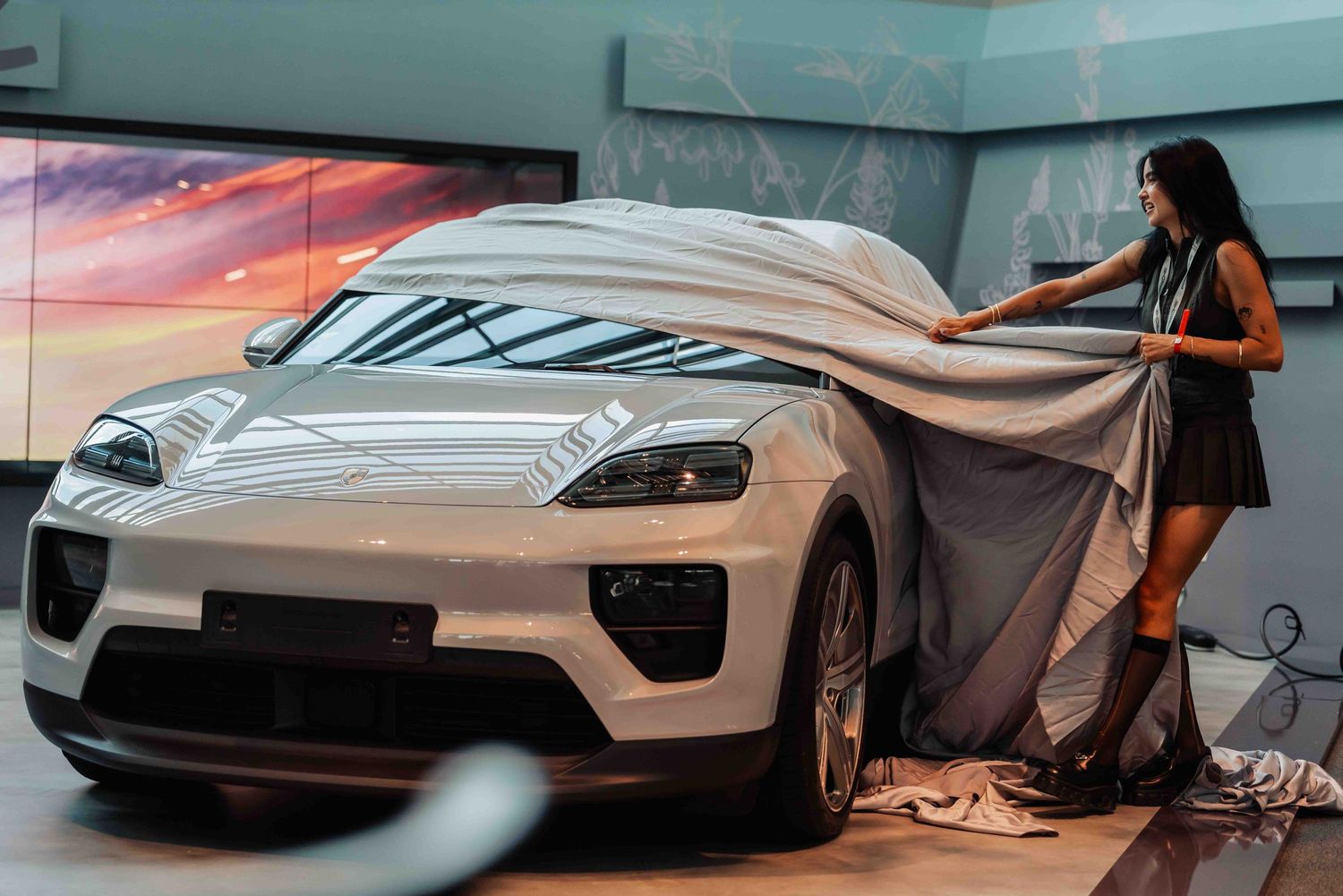Person unveiling a covered luxury vehicle in a showroom with dramatic lighting.