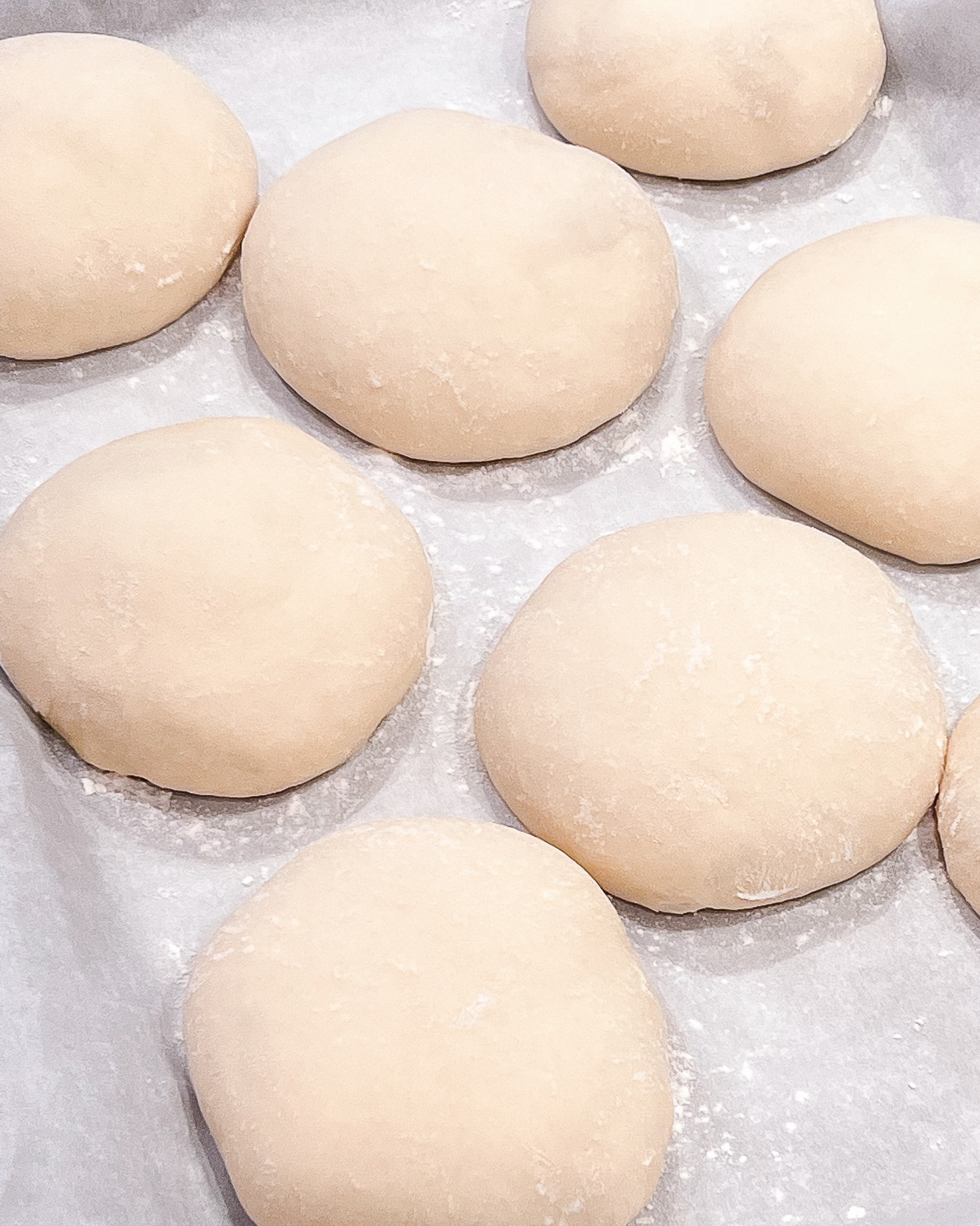 Uncooked pizza dough portions laid out on parchment paper ready for baking.