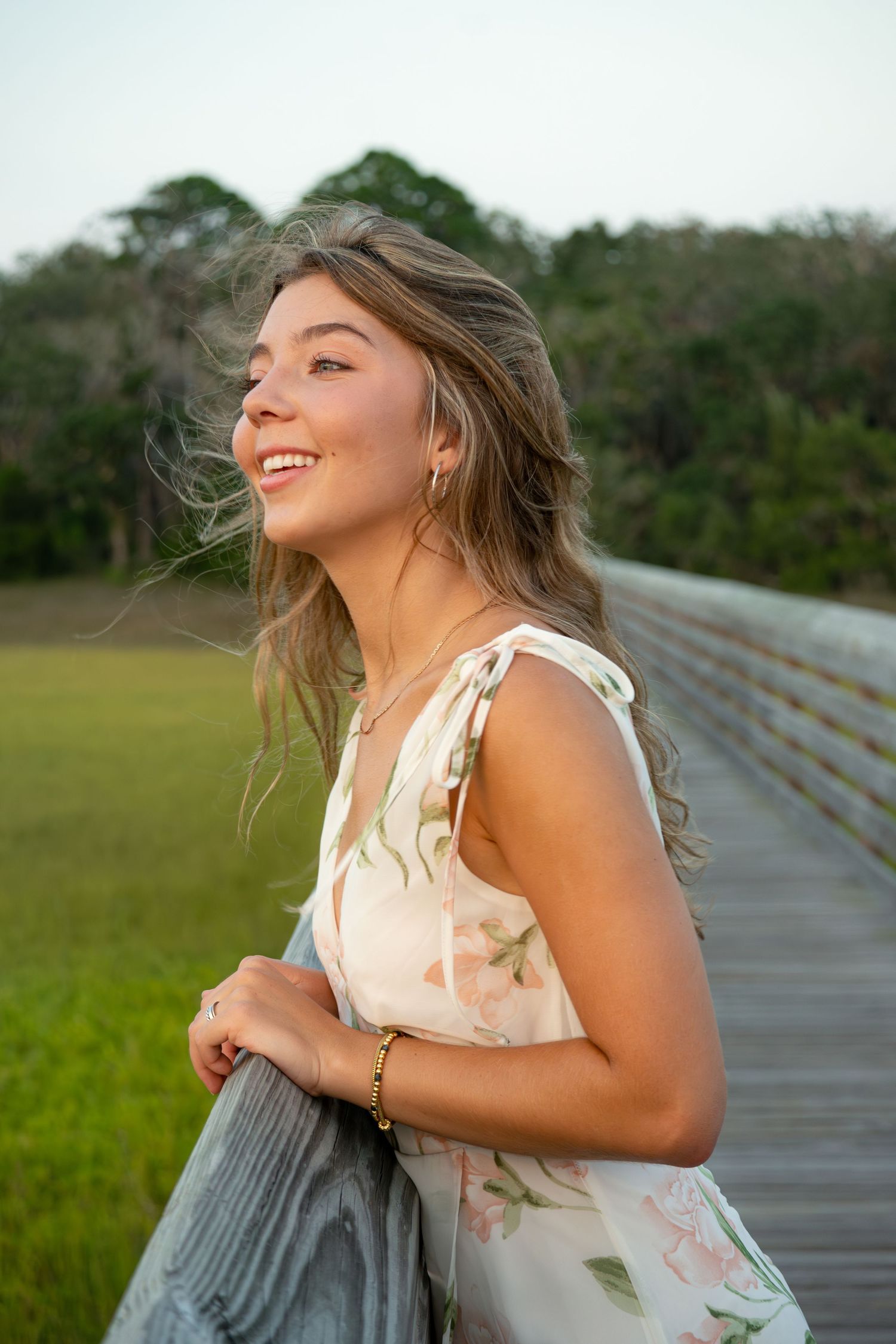 Candid portrait on wooden boardwalk with floral dress at golden hour.