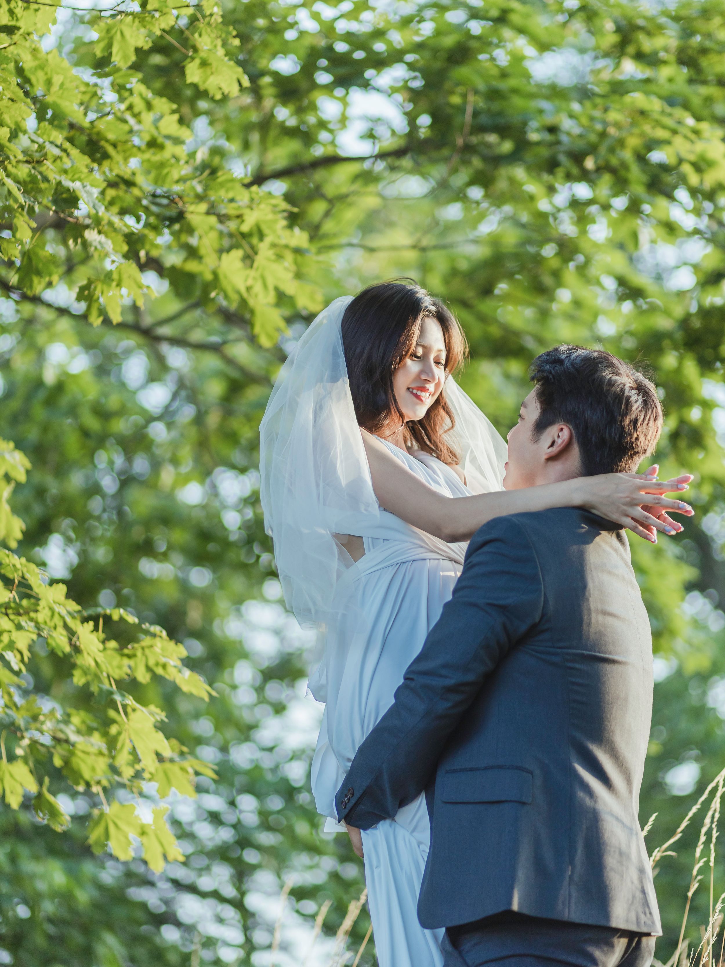A joyful wedding moment between newlyweds surrounded by green foliage in natural sunlight.