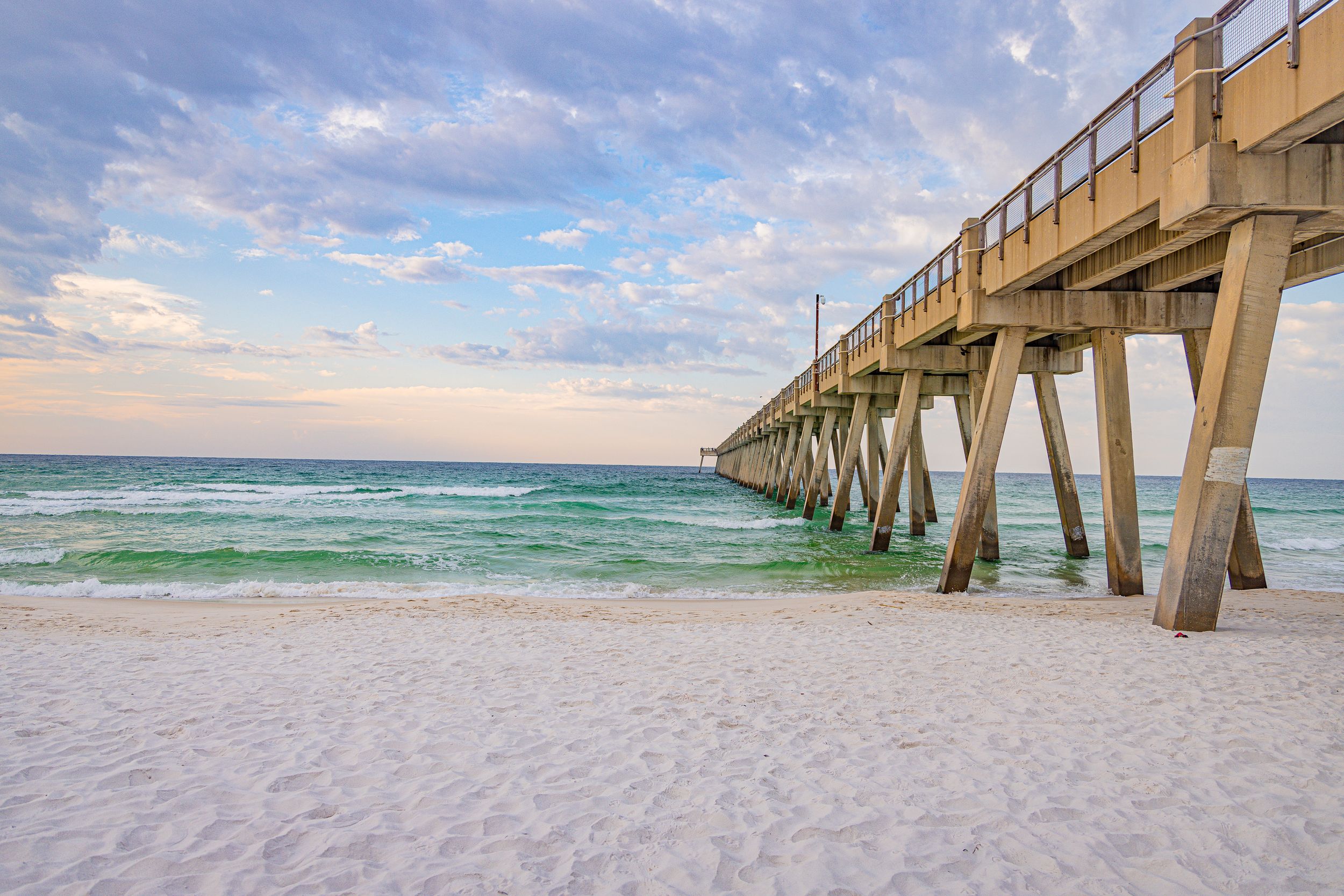 Long wooden pier stretches into emerald waters under cloudy sky at Panama City Beach.