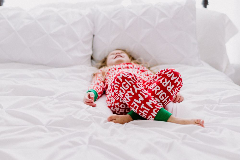 Playful moment captured laying back on white bedding in festive red pajamas. family photography