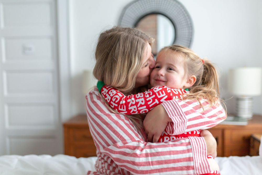 Sweet cuddle moment in matching red and white striped holiday pajamas on bed.
