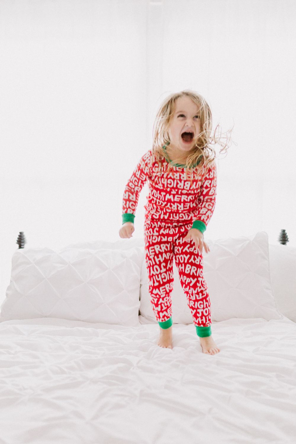 Energetic jump on white bedding while wearing red and white holiday pajamas.
family photography