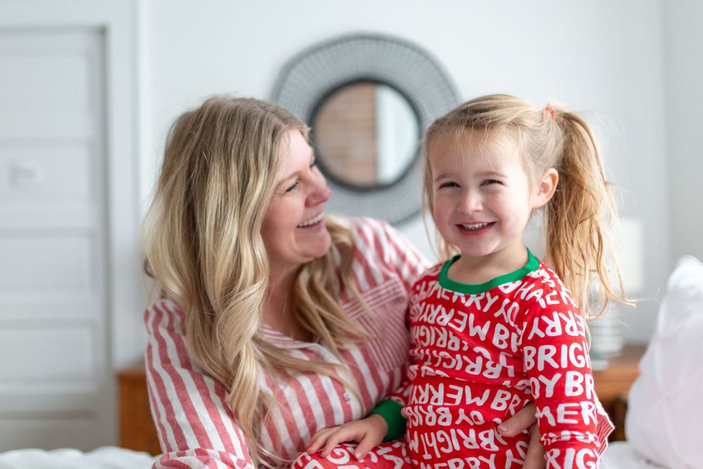 Matching holiday pajamas moment on white bed with circular mirror in background.