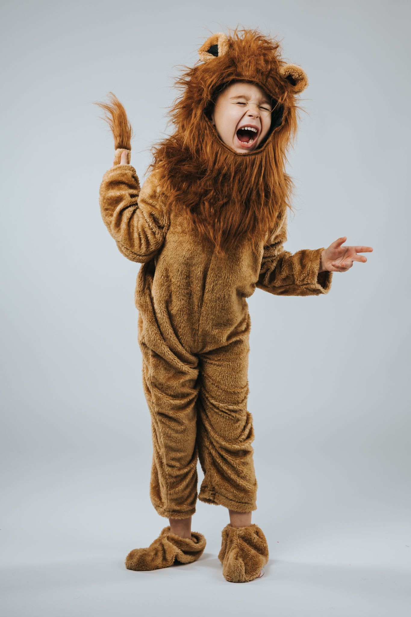 Child in furry lion costume expressing joy against grey background.