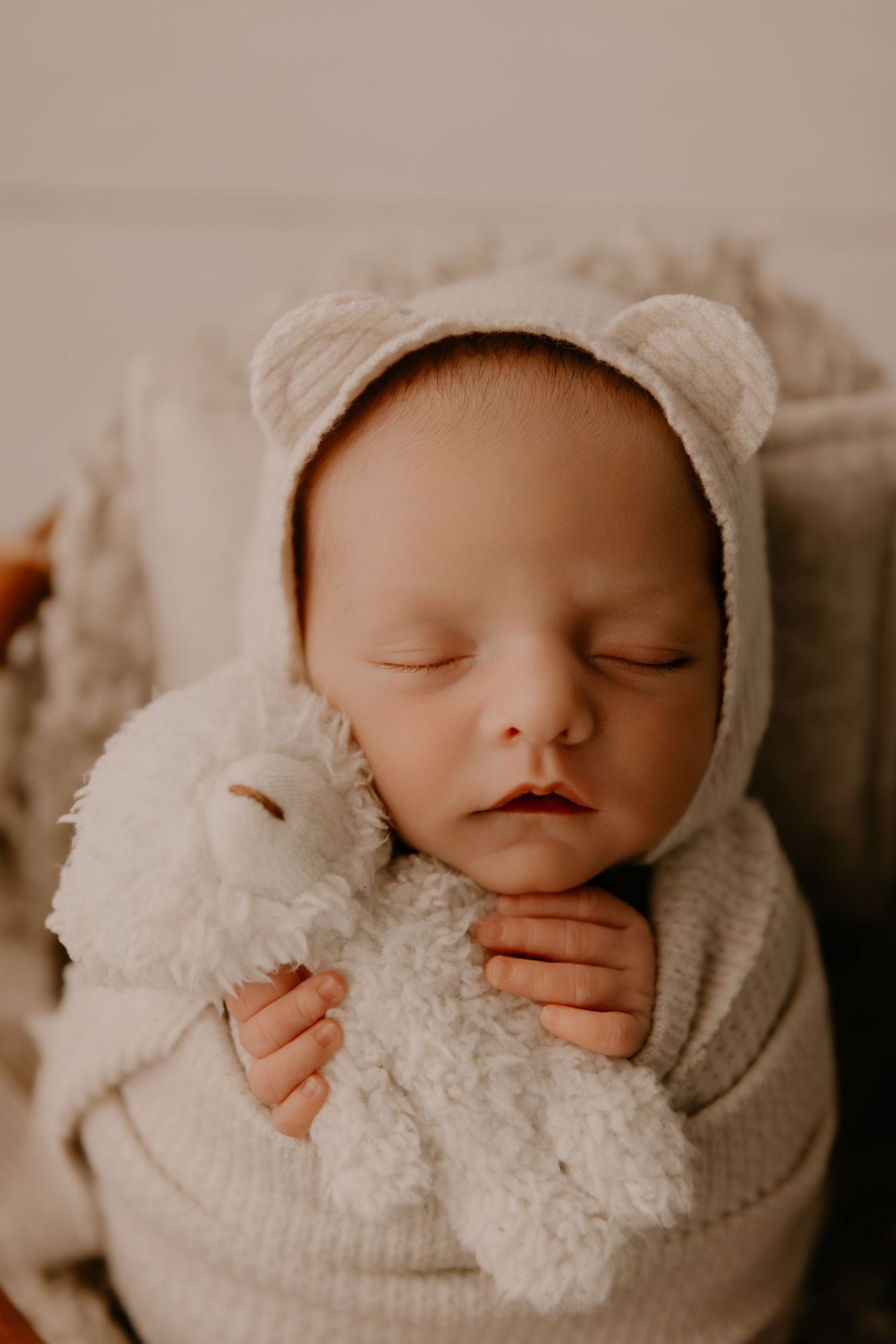 Sleeping newborn in white knit outfit with delicate headband on wooden surface.