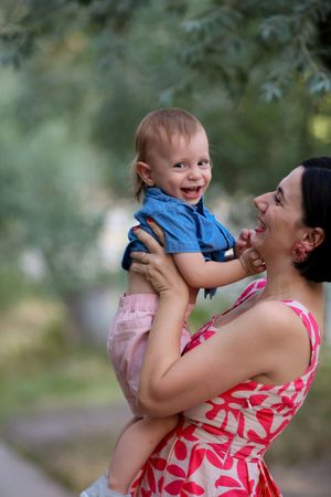 Parent and baby sharing joyful moment outdoors in summer attire.