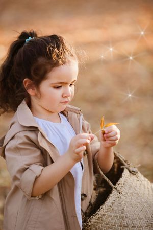 Child in beige coat examines something magical with sparkles in warm autumn lighting.