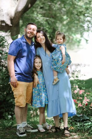 Family of four wearing coordinating blue and floral outfits pose together in a garden setting.