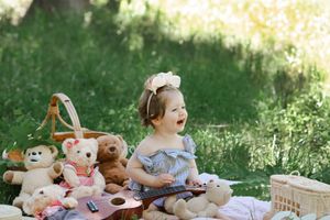 Child having a teddy bear picnic outdoors with multiple stuffed animals on a blanket.