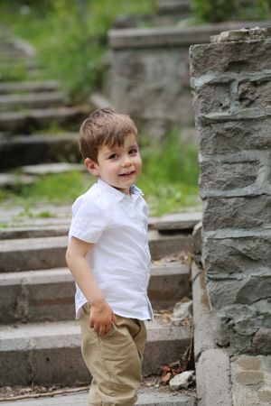 Young child in white shirt and khaki pants stands on stone steps outdoors.