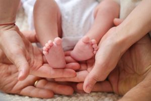 Tiny newborn feet cradled gently in adult hands on white fabric.
