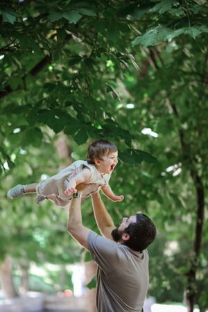Playful moment in a lush green park as child is lifted high into the air.