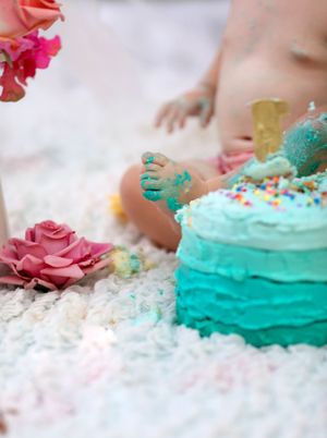 Messy turquoise ombre cake with pink flowers and tiny feet covered in frosting.