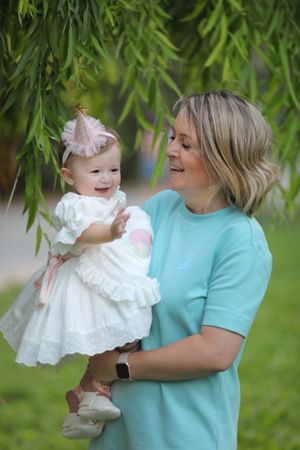 Outdoor portrait under willow tree branches with white dress and pink hair bow.