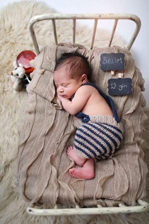 Sleeping newborn in striped shorts on textured knit blanket with small chalkboard signs.
