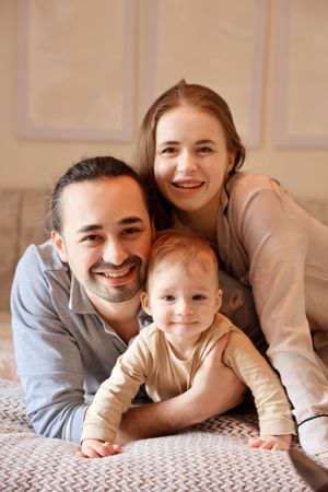 A cozy family portrait on bed with warm lighting and neutral tones.