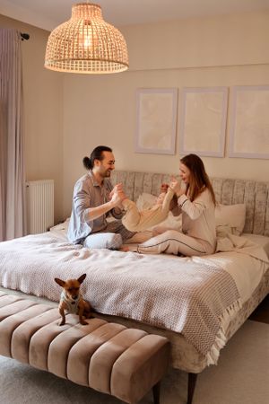 A couple enjoying a playful moment on their bed while a toy fox sits at the foot.