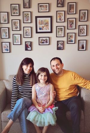 A family sitting on a couch with a wall of framed photos behind them.