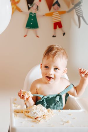 Joyful baby in a high chair playing with food and making a happy mess.