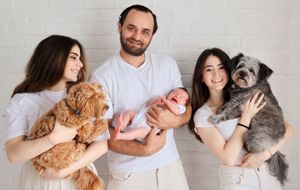 Happy family posing with their newborn baby and two pets against white background.