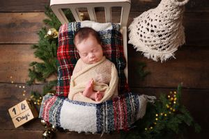 Sleeping newborn on plaid blanket in wooden crate with Christmas decorations.