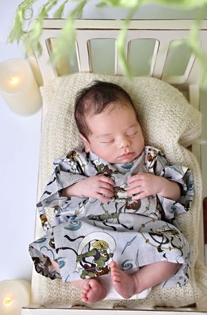 Peaceful sleeping baby in dinosaur print pajamas on white chair with candle nearby.
