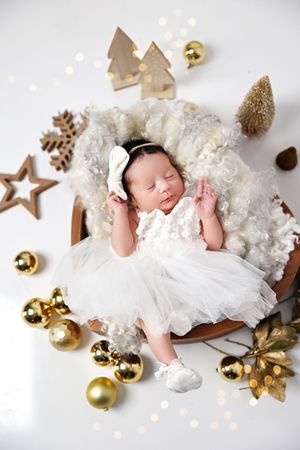 Newborn sleeping peacefully among Christmas decorations with gold ornaments and wooden trees.