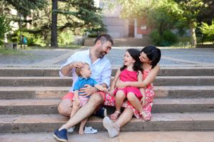 Family sharing laughs while sitting together on outdoor stairs.
