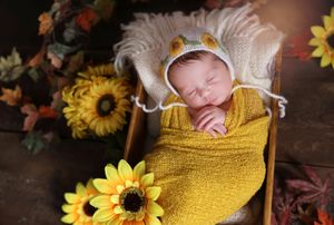 Sleeping newborn wrapped in yellow swaddle surrounded by sunflowers in rustic setting.