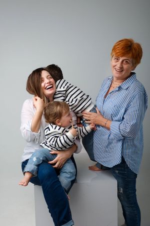 Candid family moment with three generations sharing laughter against grey background.